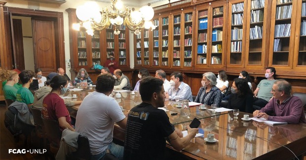 En la imagen se observa una vista panorámica de la Biblioteca de FCAG con las y los Consejeros Directivos sentados alrededor de la mesa de madera y con el Decano, la Secretaria Académica y la Vice Decana, en la punta de la mesa.